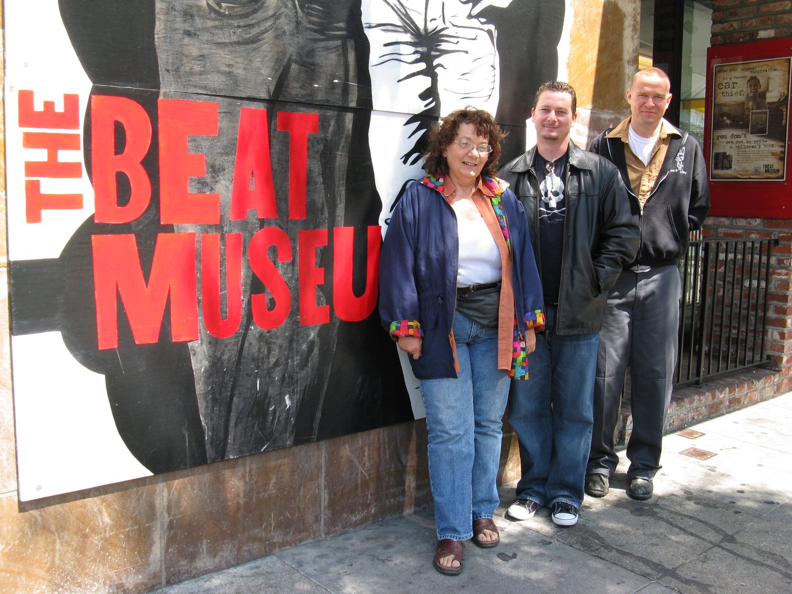 Linda King and Matt Sesow with a friend outside The Beat Museum, San Francisco, under a large red painted sign