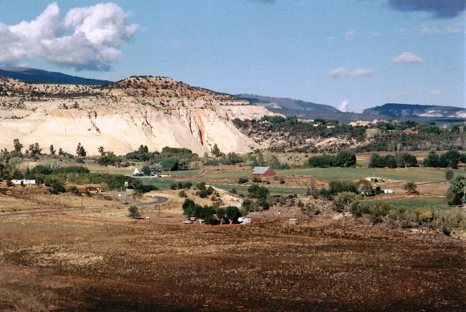 Wide view of Boulder, Utah: green fields below pale sandstone cliffs