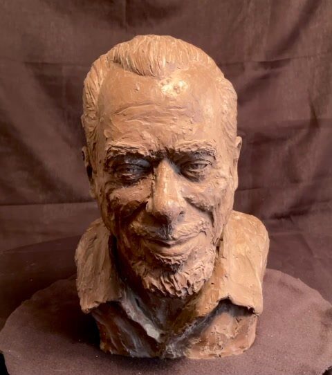 Clay-colored sculpted head of Charles Bukowski, grinning