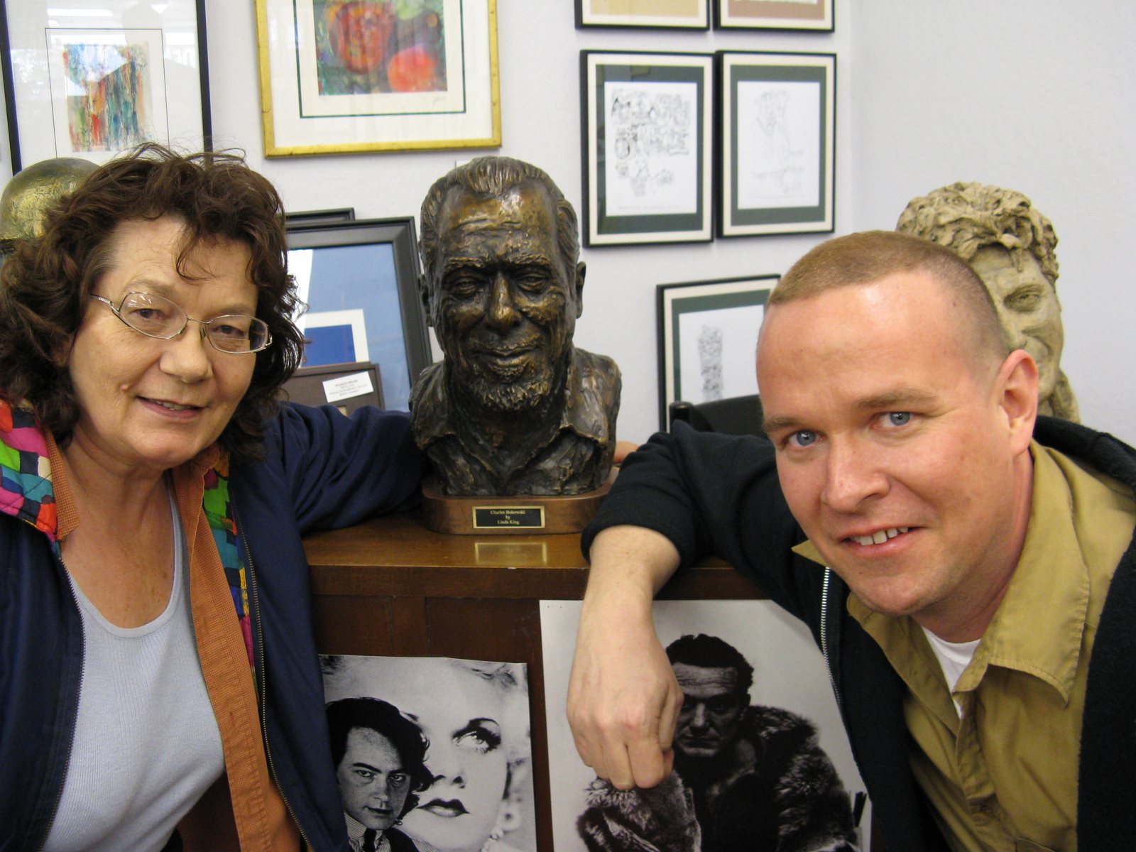 Linda King and Matt Sesow on either side of her bronze bust of Charles Bukowski; the plaque reads Charles Bukowski by Linda King