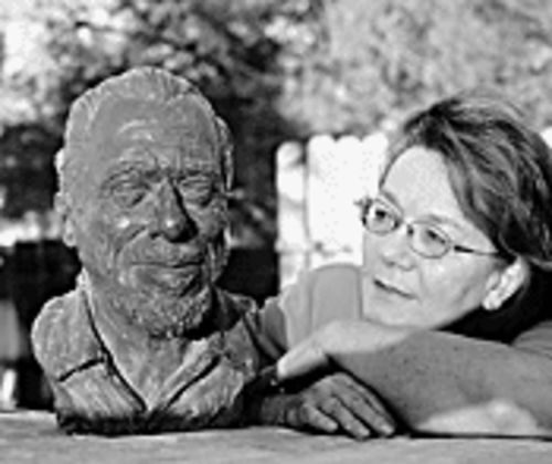 Black and white photo of Linda King resting her chin beside her sculpted head of Charles Bukowski