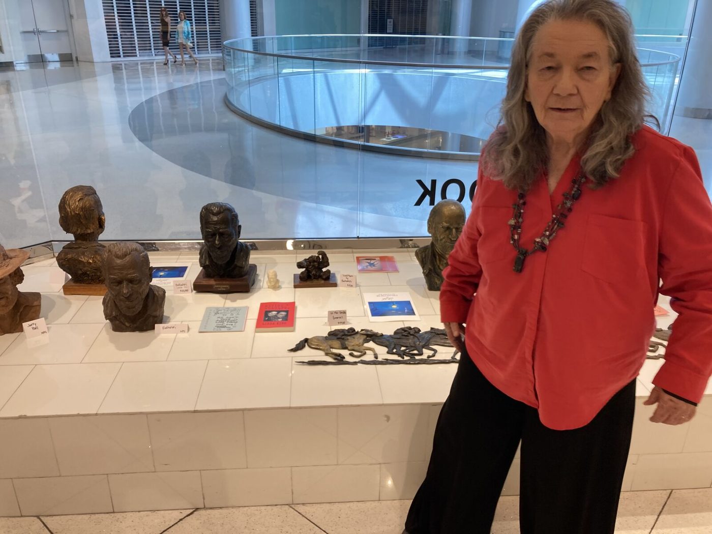 Linda King in a red shirt beside a row of bronze busts