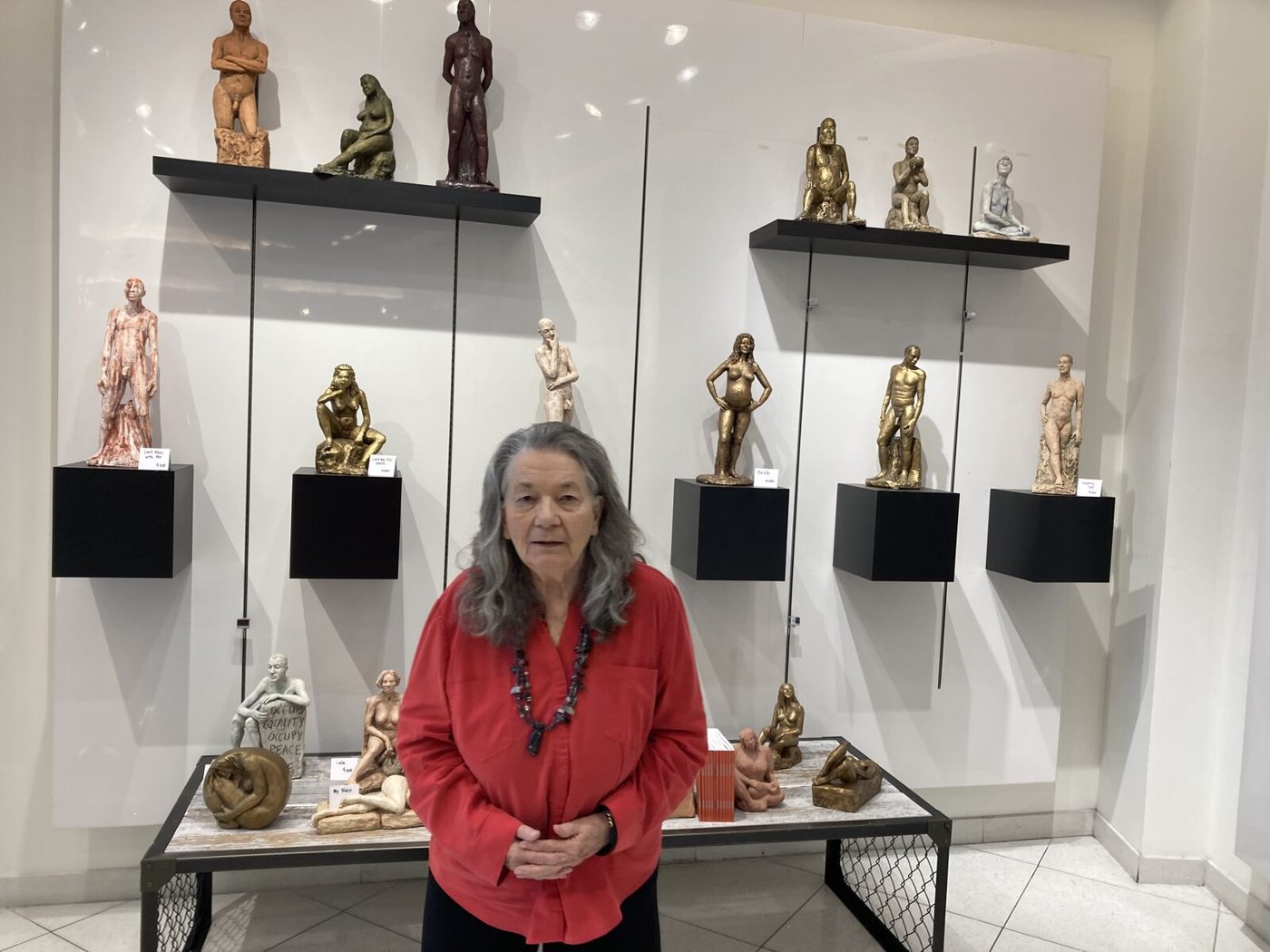 Linda King standing below shelves of small sculptures